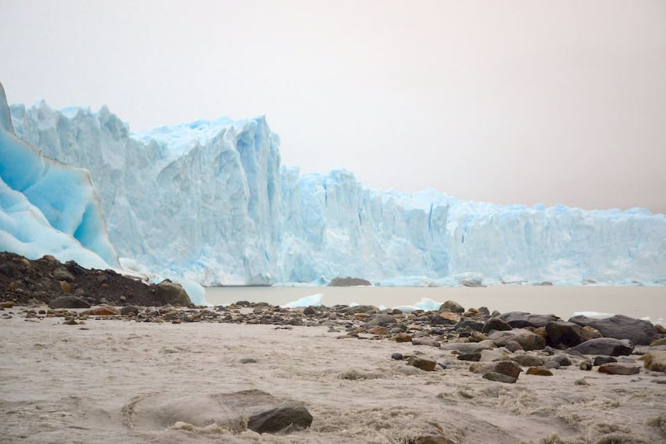 Un glacier avec un paysage rocheux au premier plan et une étendue d'eau calme en arrière-plan.