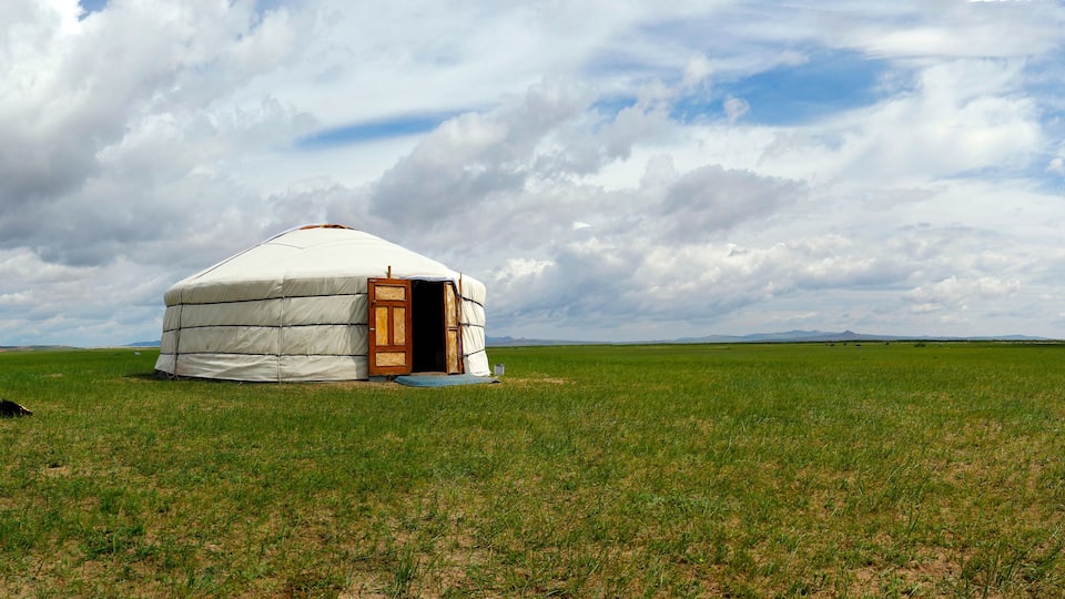 A yurt in a grassy field with mountains in the background.