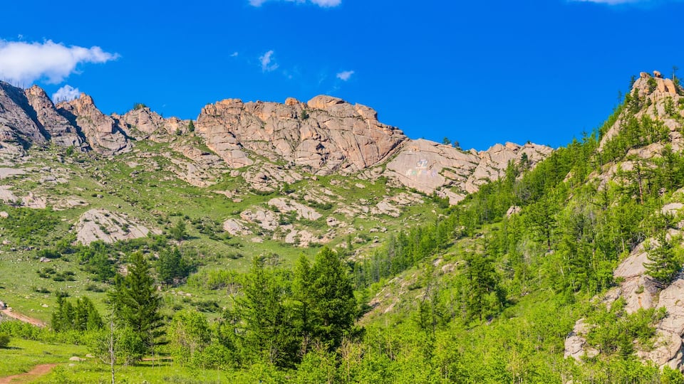 A mountainous landscape with rocky peaks, green vegetation, and a small building.