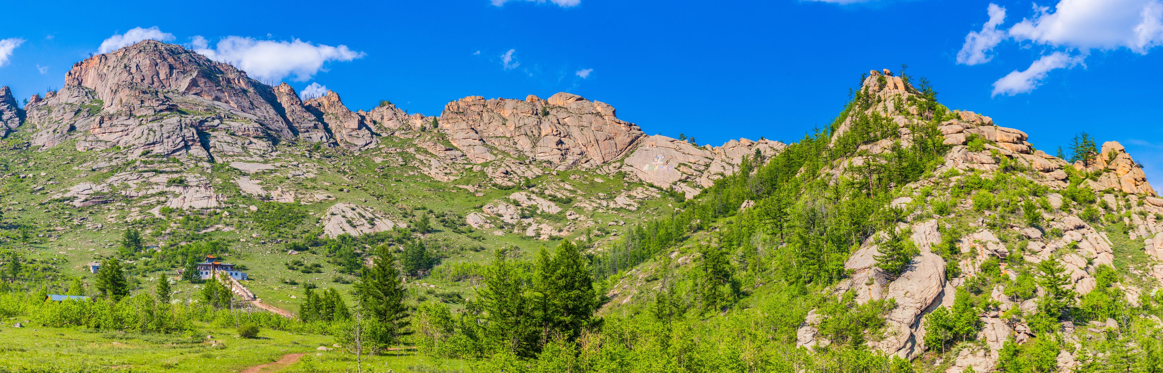A mountainous landscape with rocky peaks, green vegetation, and a small building.