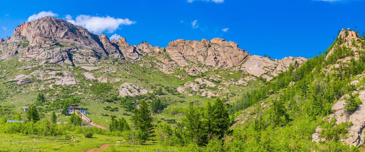 A mountainous landscape with rocky peaks, green vegetation, and a small building.