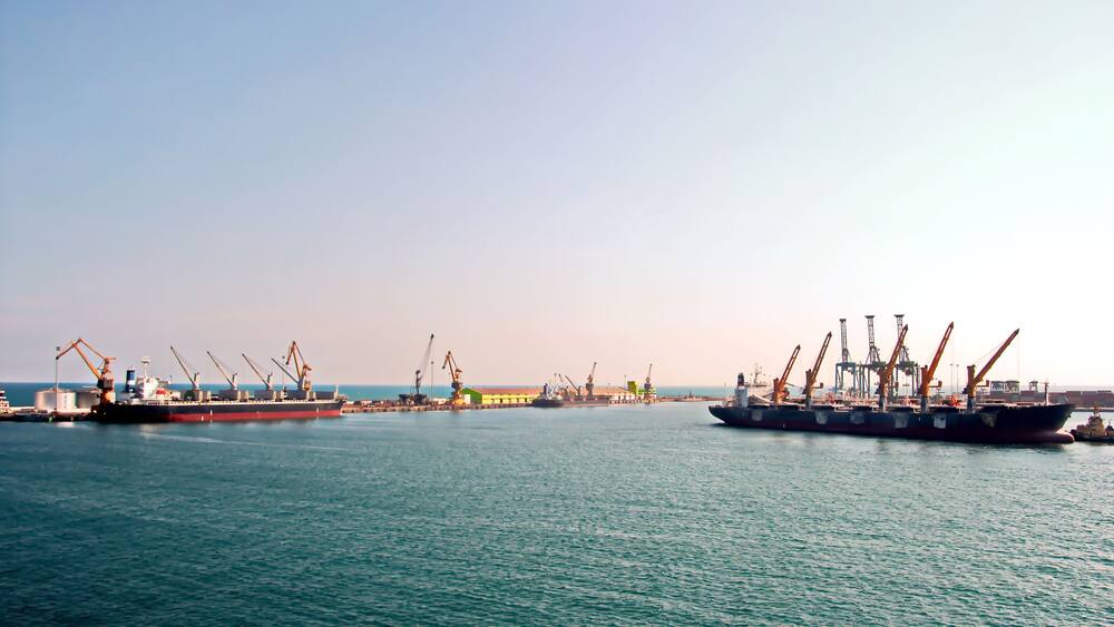 A harbor with large cargo ships and cranes.