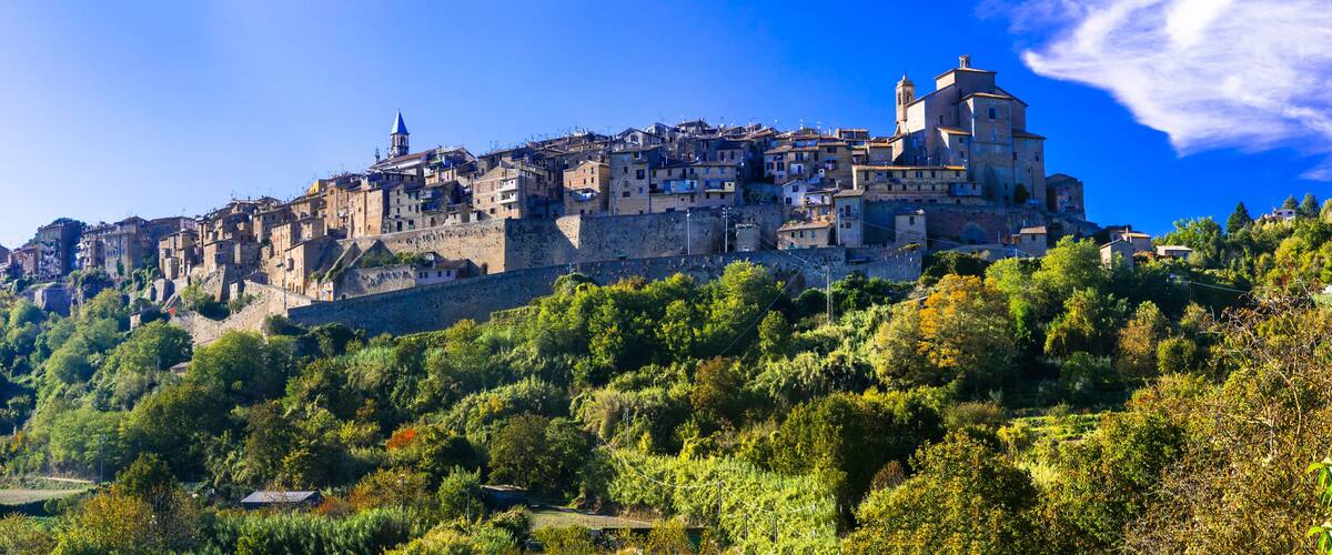 A historic walled town with a prominent church on a hill, surrounded by lush greenery.