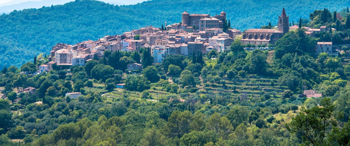 A historic town nestled in a valley with terraced fields, surrounded by lush green hills and mountains.