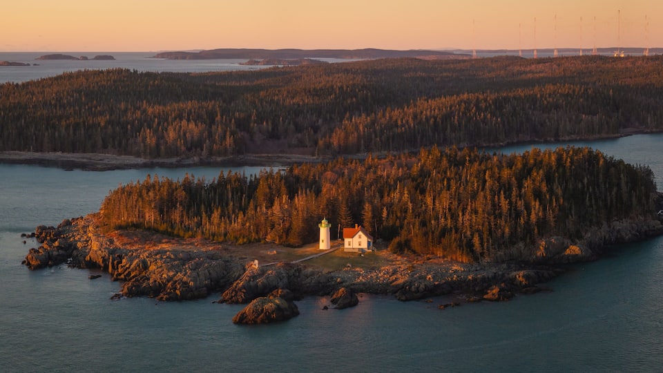A lighthouse on a rocky island surrounded by dense forest and calm waters.