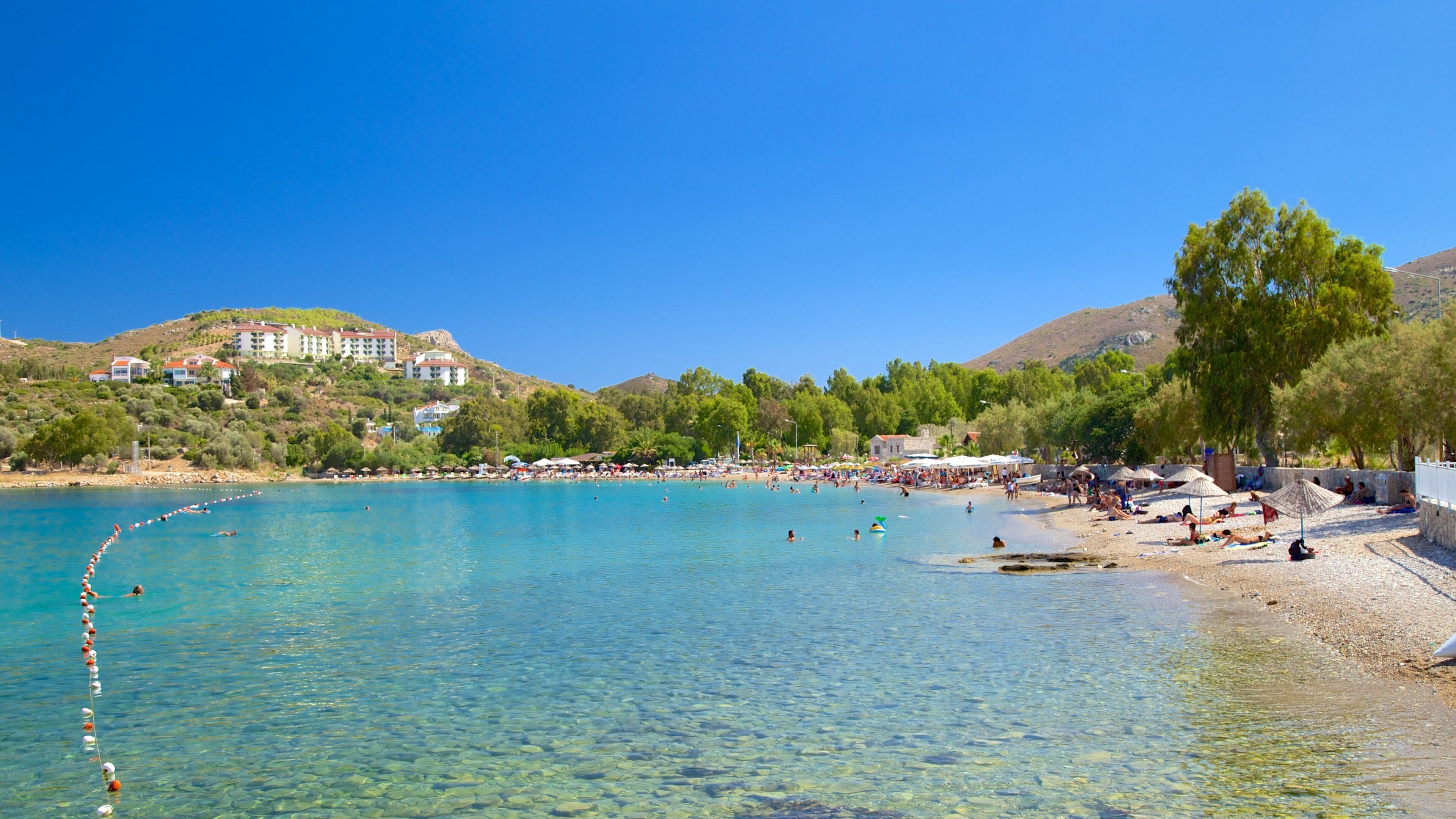 A clear blue sea with a pebble beach, umbrellas, and people sunbathing.