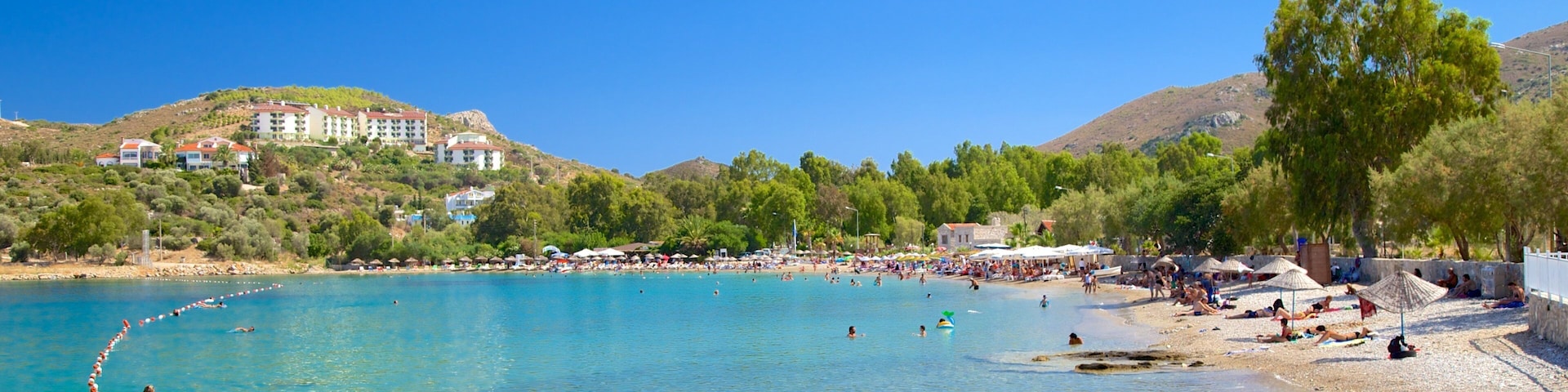 A clear blue sea with a pebble beach, umbrellas, and people sunbathing.