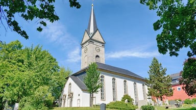 A church with a tall steeple and a clock tower, surrounded by trees and a cemetery.