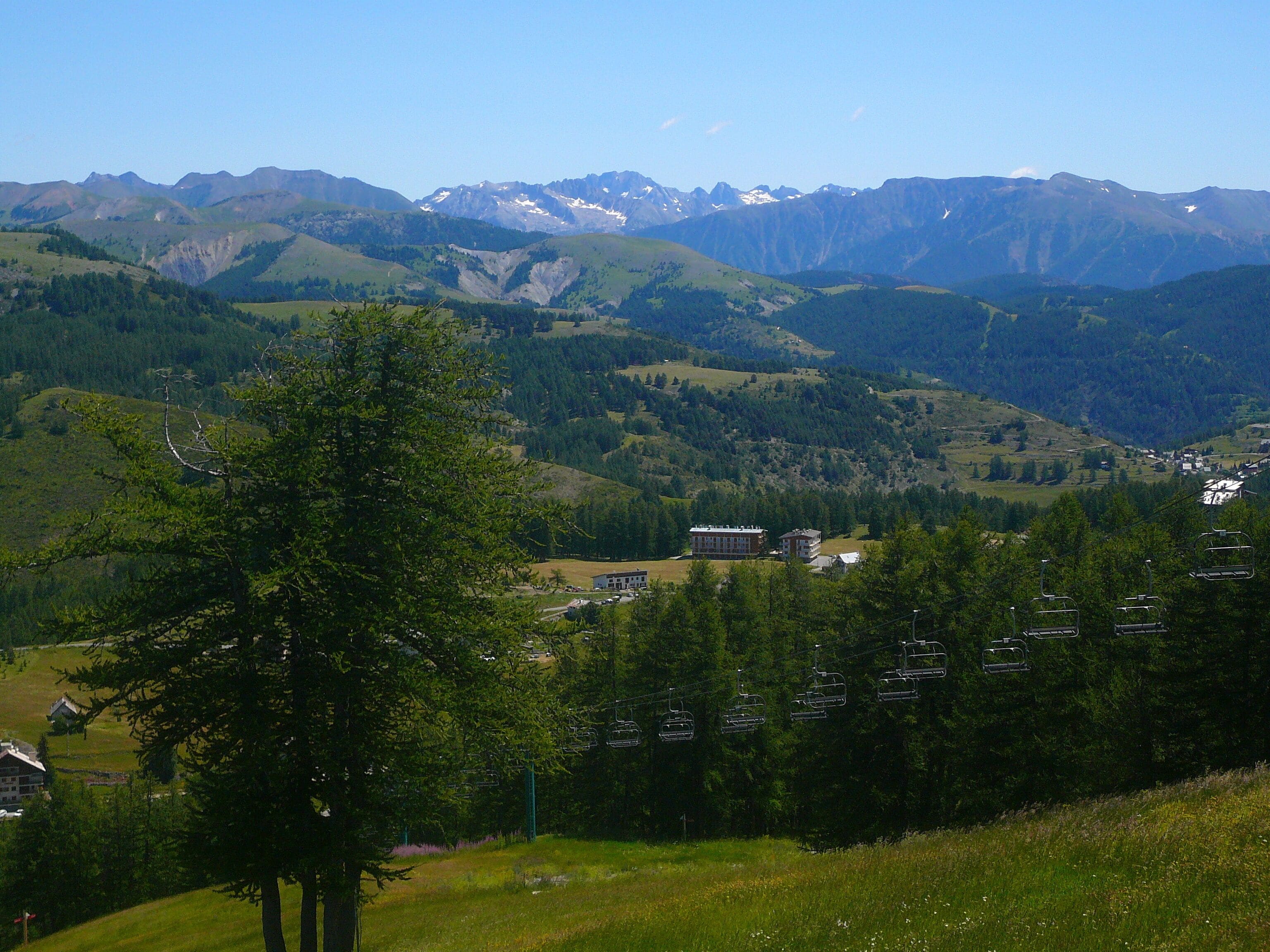 A mountainous landscape with a ski lift, houses, and a clear sky.