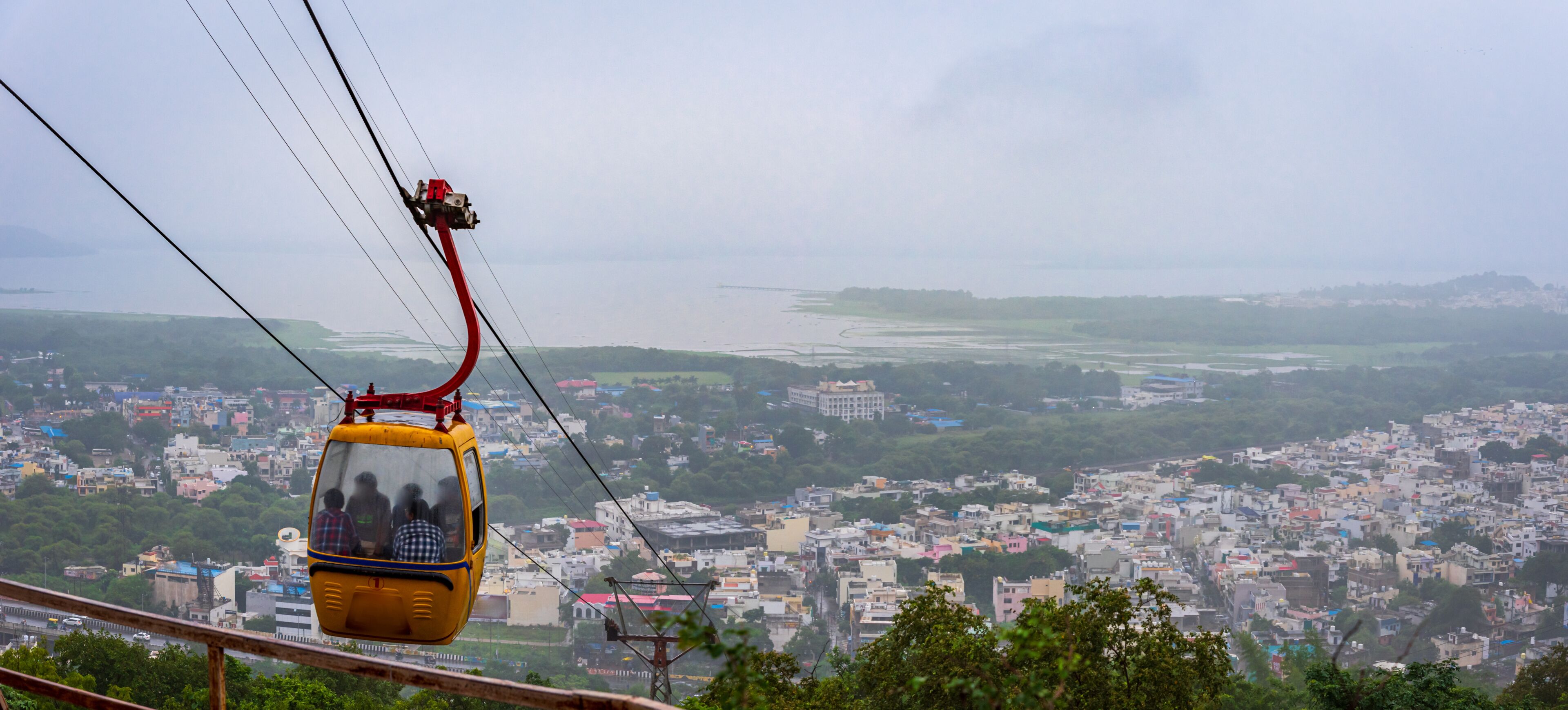 A cable car with passengers, a cityscape, and a river in the background.