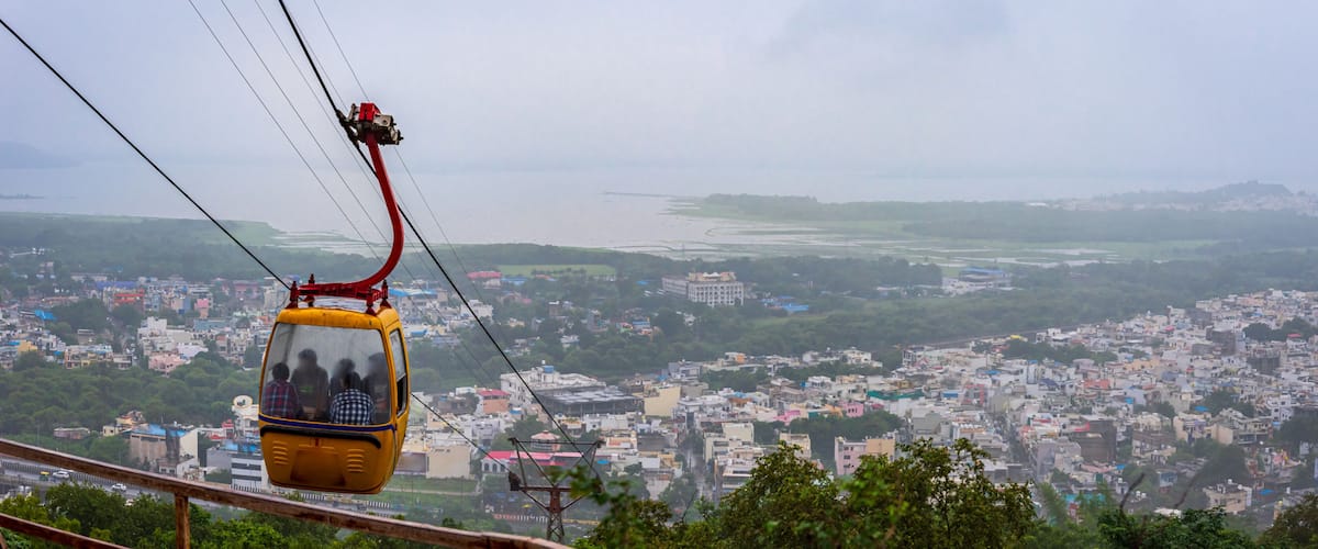 A cable car with passengers, a cityscape, and a river in the background.