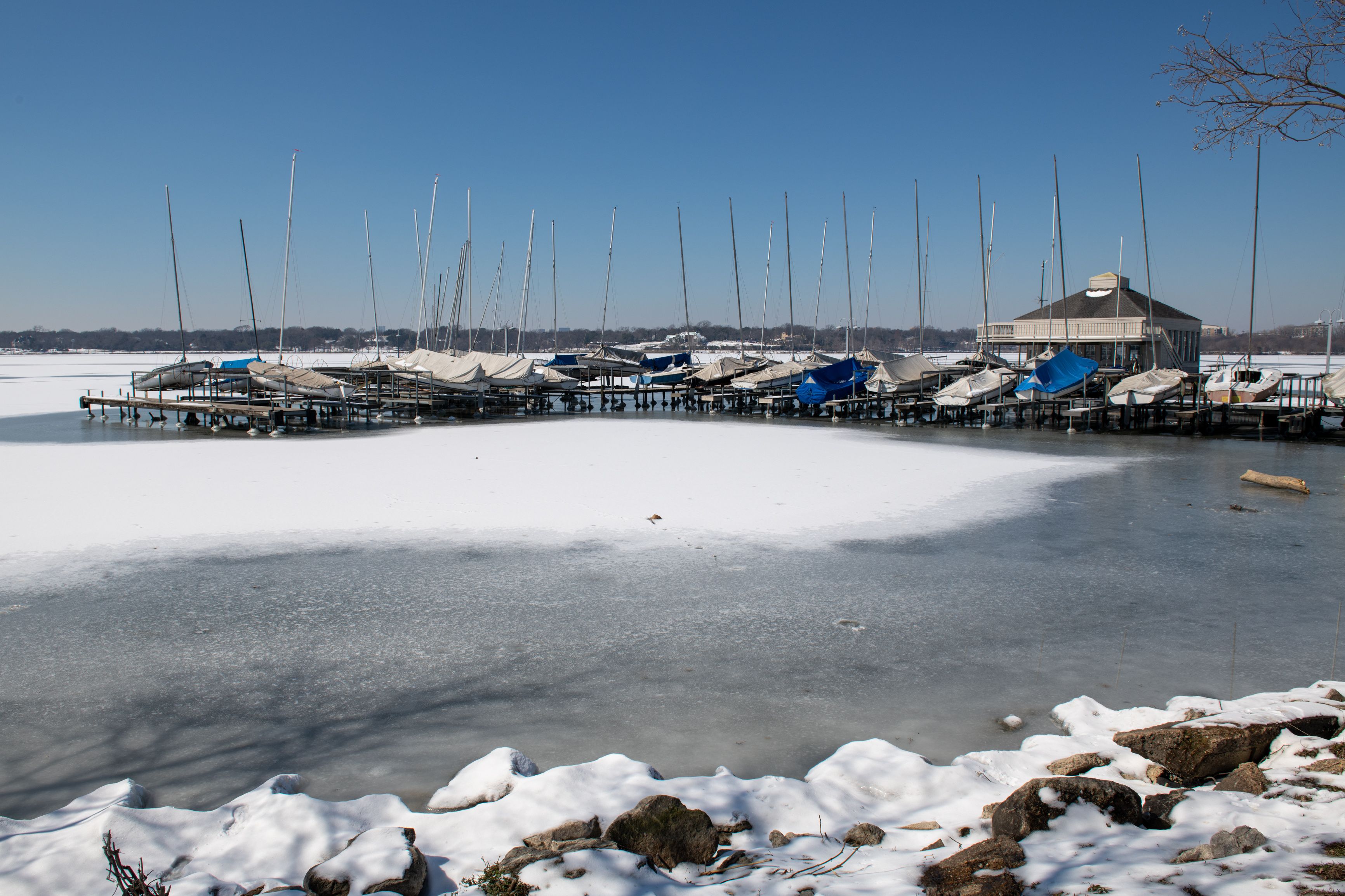 A frozen lake with sailboats docked on piers and a building in the background.