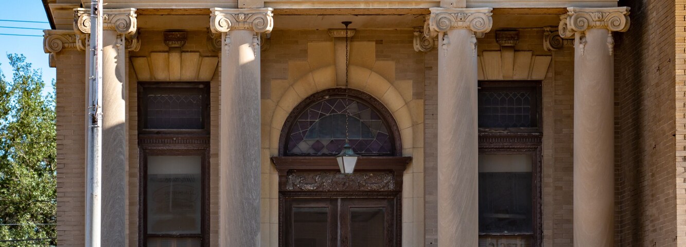 A classical building with 'FIRST NATIONAL' inscribed on the facade, featuring a symmetrical entrance with columns, a central pediment, and a decorative balcony.