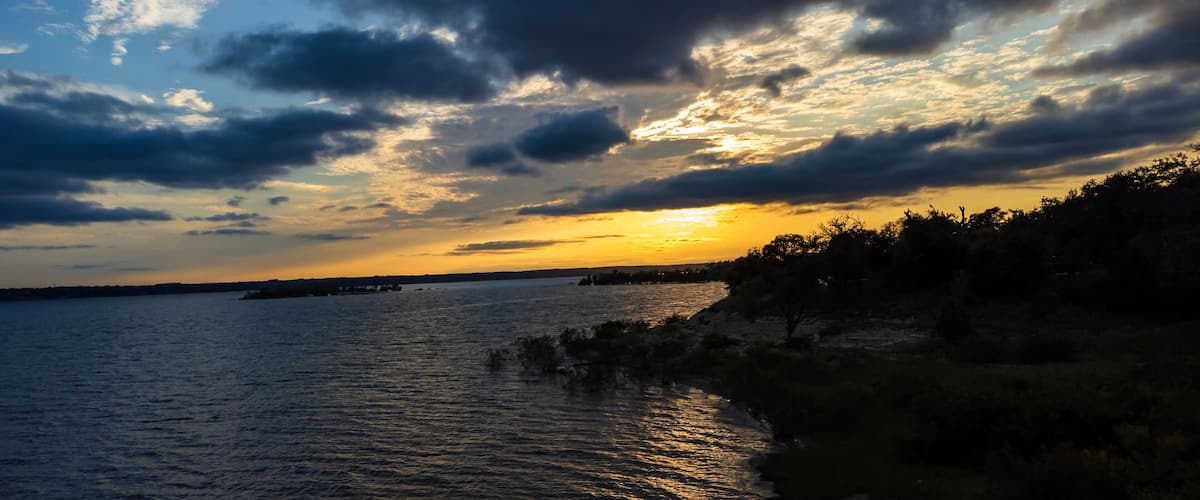 A sunset over a body of water with a rocky shoreline and a distant landmass.