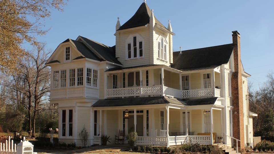 A large, white, two-story house with a black roof and multiple windows.