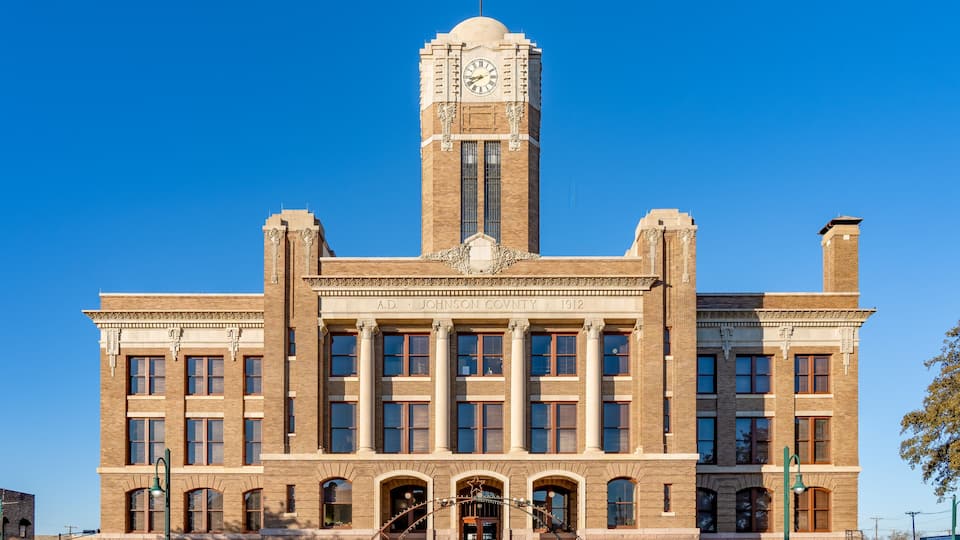 A large brick building with a clock tower, columns, and a sign reading 'A.D. Johnson County 1912'.