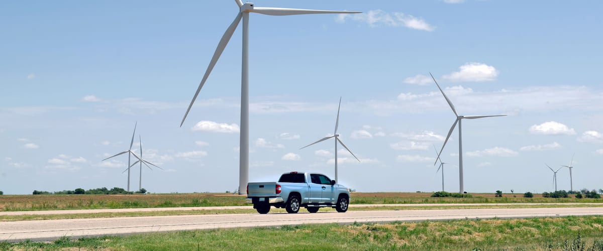 A silver pickup truck on a road with wind turbines in the background.
