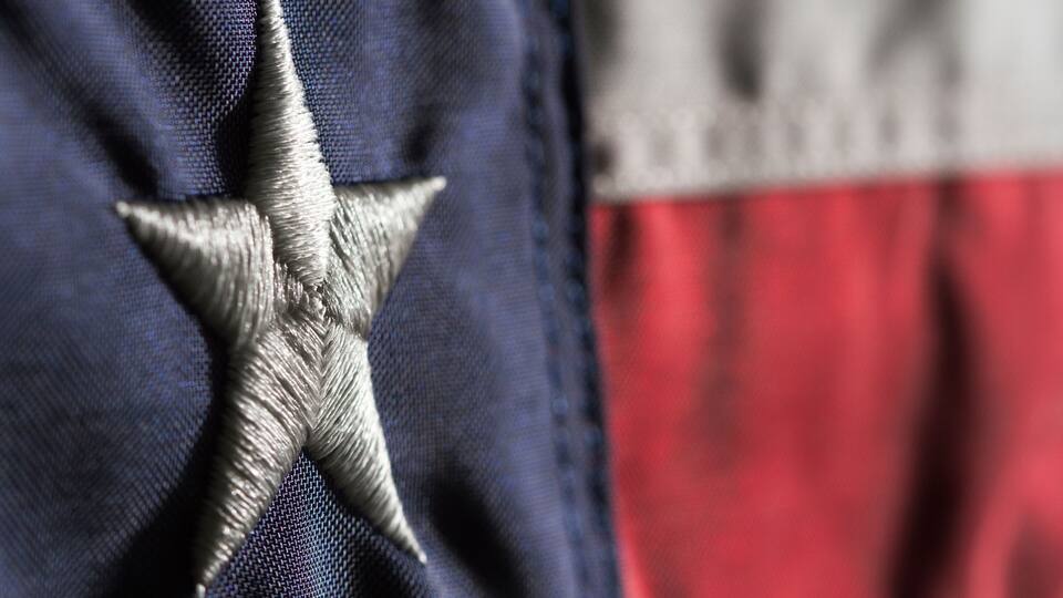 A close-up of a flag with a silver star on a blue field and red and white stripes.