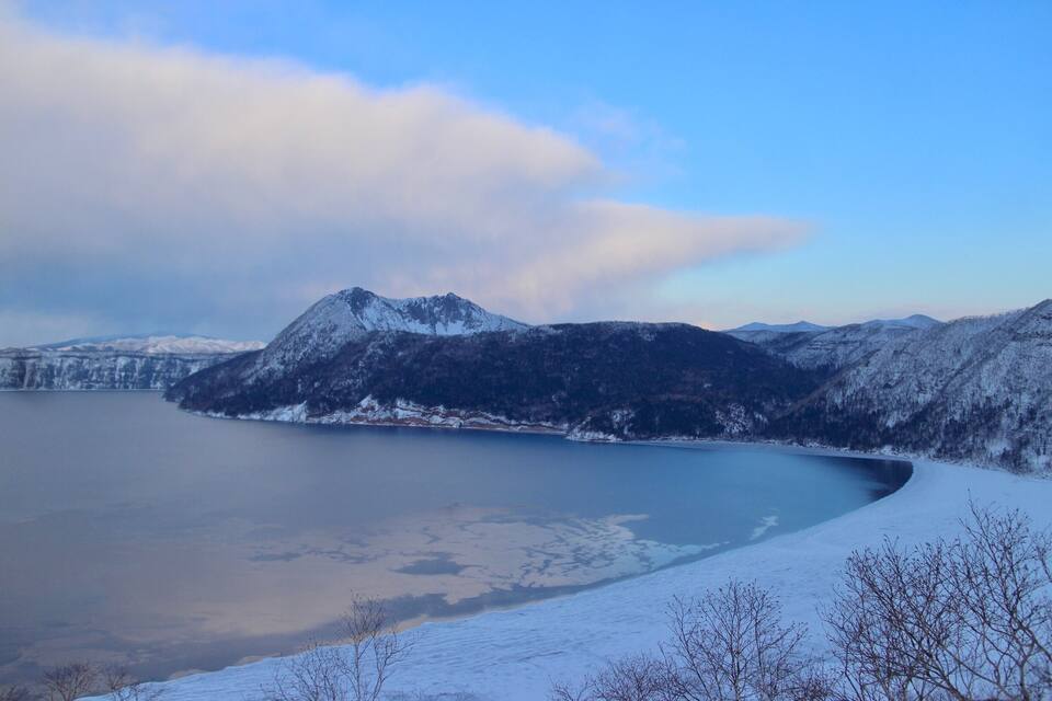A snow-covered mountain range with a lake in the foreground.