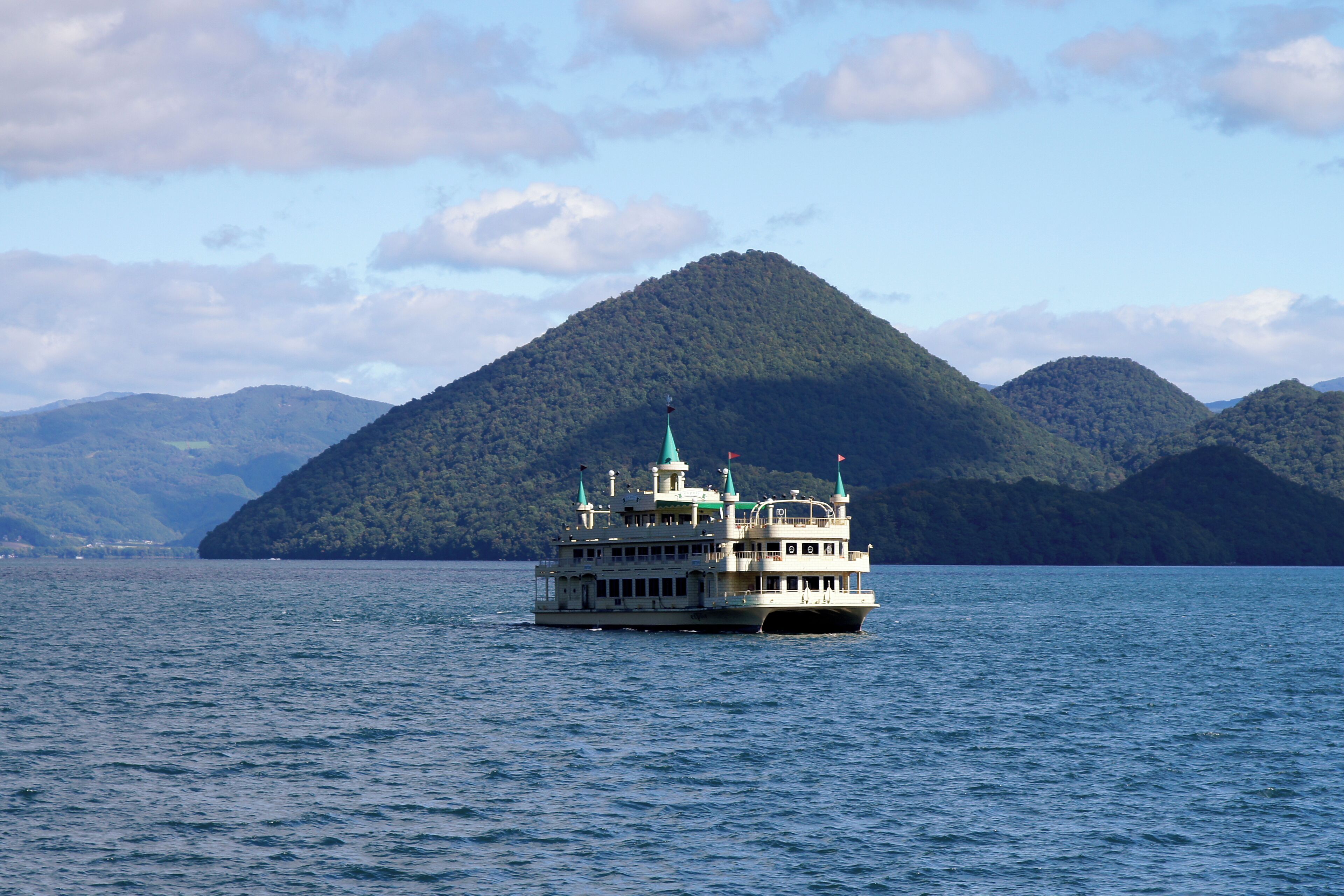 A riverboat on a calm river with a forested island in the background.