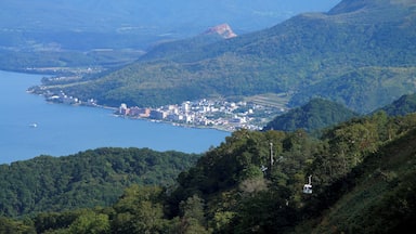 Un pueblo costero ubicado entre montañas, con una gran masa de agua a la izquierda y densas colinas boscosas.