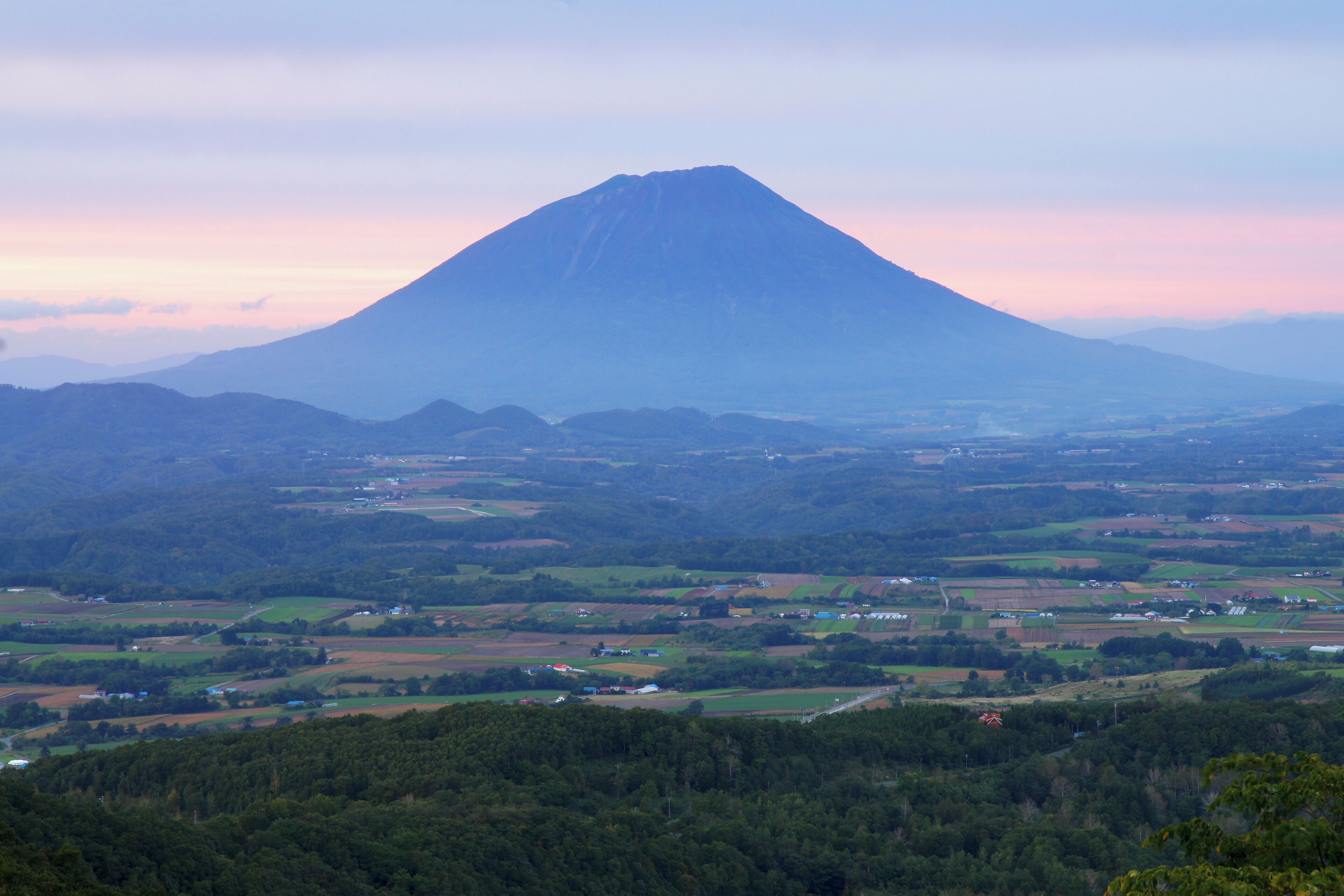 A mountain landscape with a prominent peak, surrounded by green fields and scattered buildings.