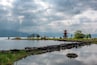 A tranquil lakeside scene with a traditional red pagoda, rocky shoreline, and distant mountains under a cloudy sky.