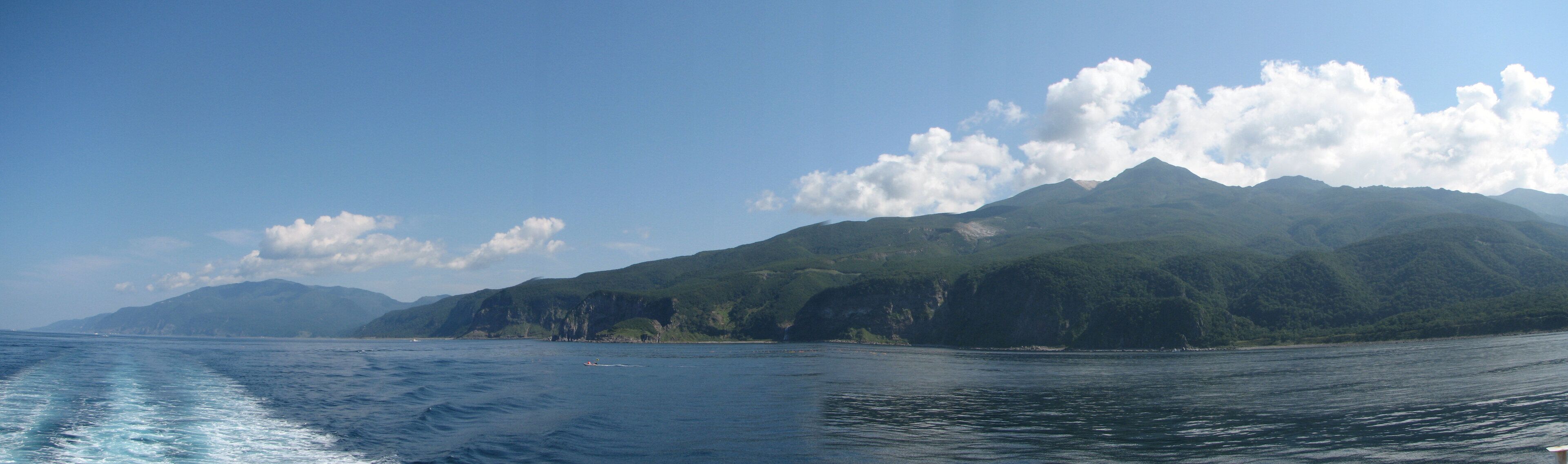A coastal landscape with a mountain range and a clear sky.
