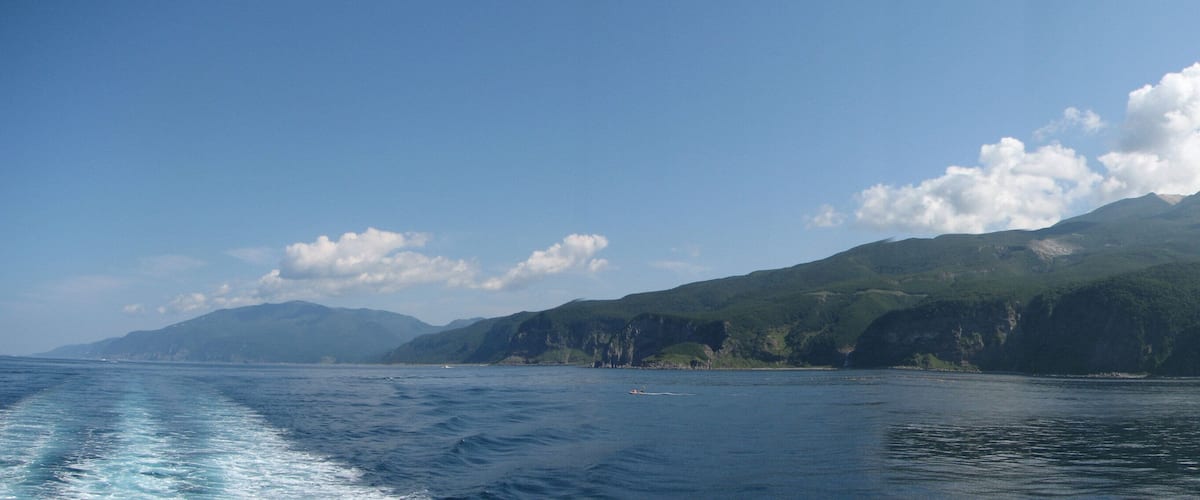 A coastal landscape with a mountain range and a clear sky.