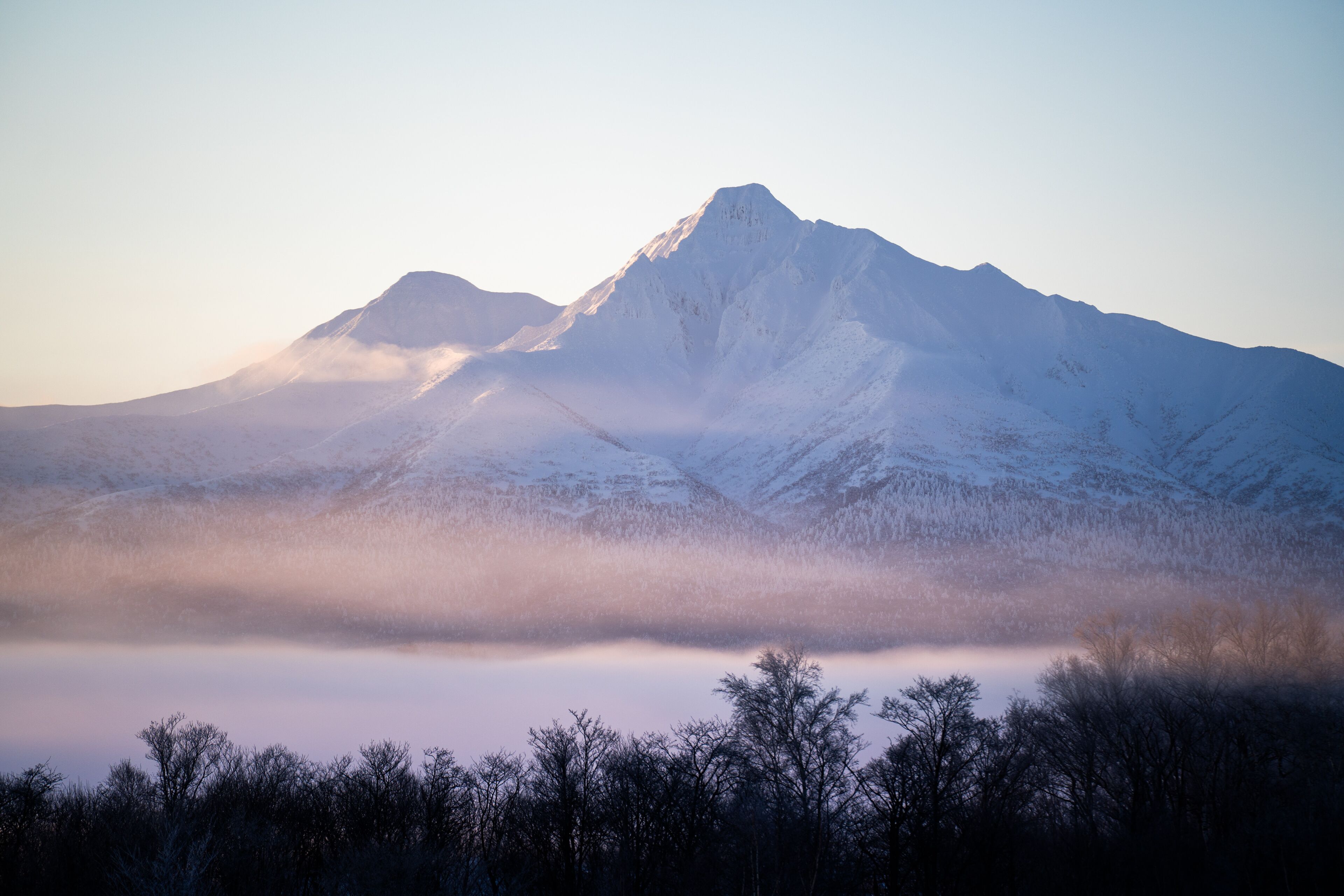 Mount Shari at sunrise in winter, Hokkaido, glowing softly above misty snowfields, capturing a serene and majestic Japanese landscape
