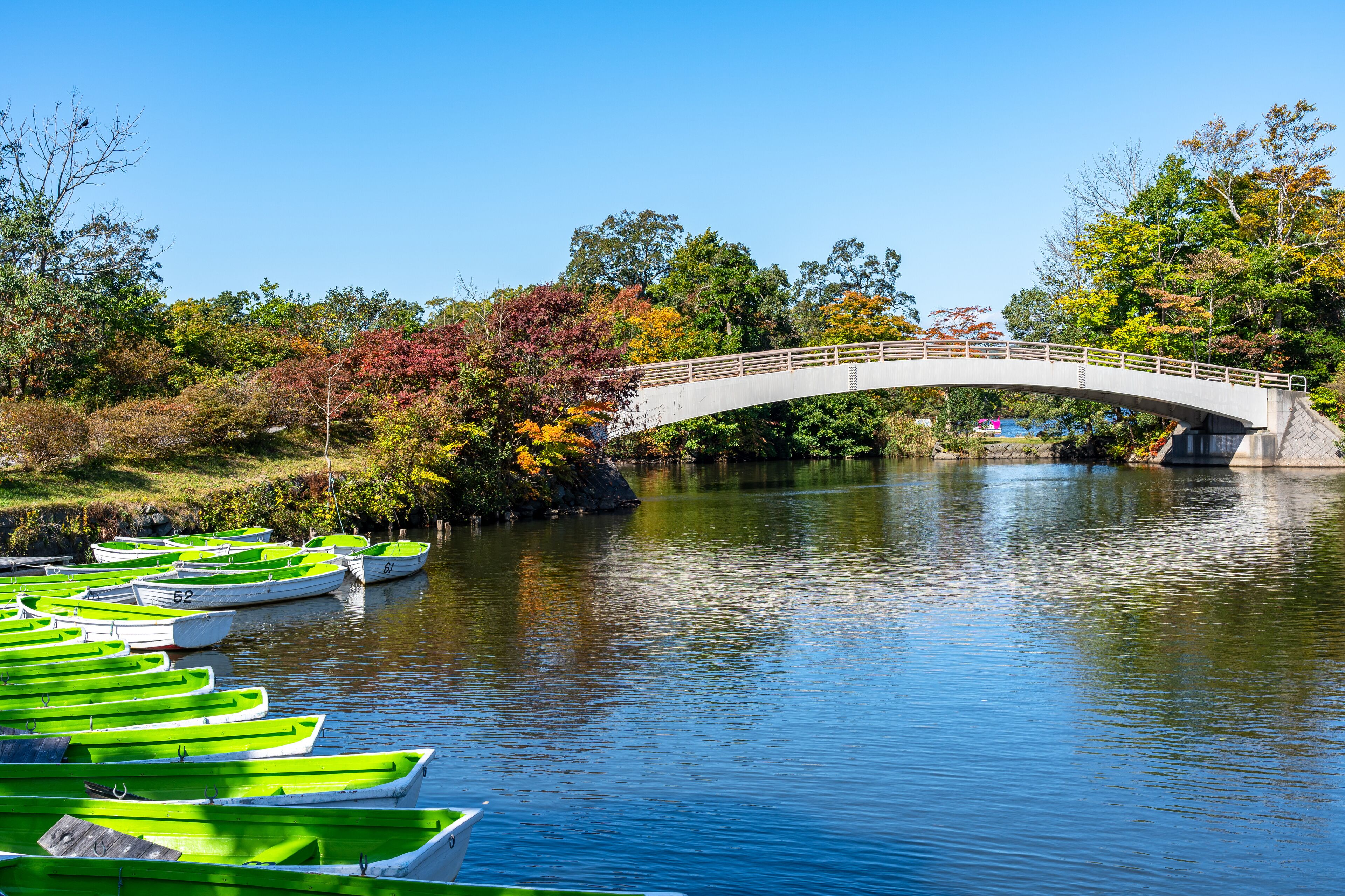 A stone bridge over a calm river with green rowboats docked on the left.