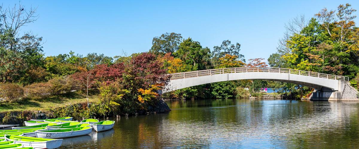 A stone bridge over a calm river with green rowboats docked on the left.