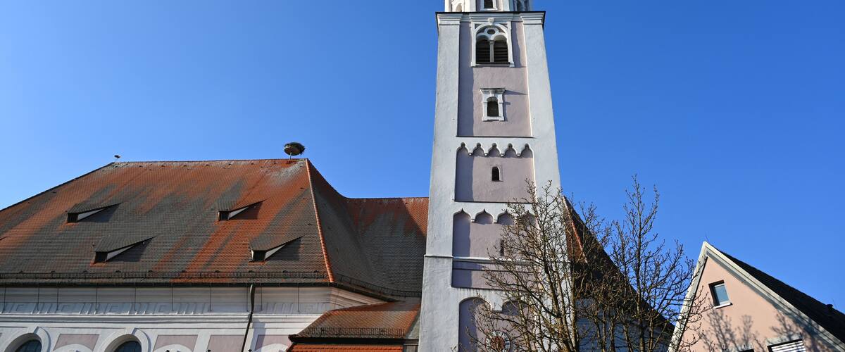 A tall church tower with a clock, a clear blue sky, and a rusted roof.