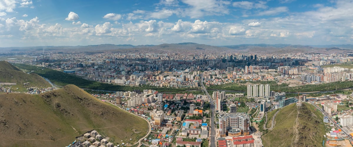 A panoramic view of a city with a river, hills, and a distant mountain range.
