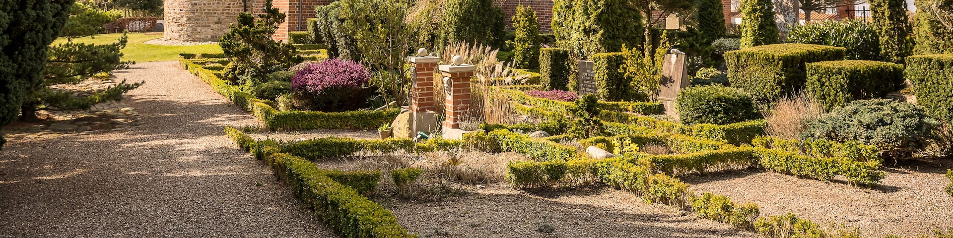 A historic brick building with a tower, surrounded by well-manicured gardens and tall trees.