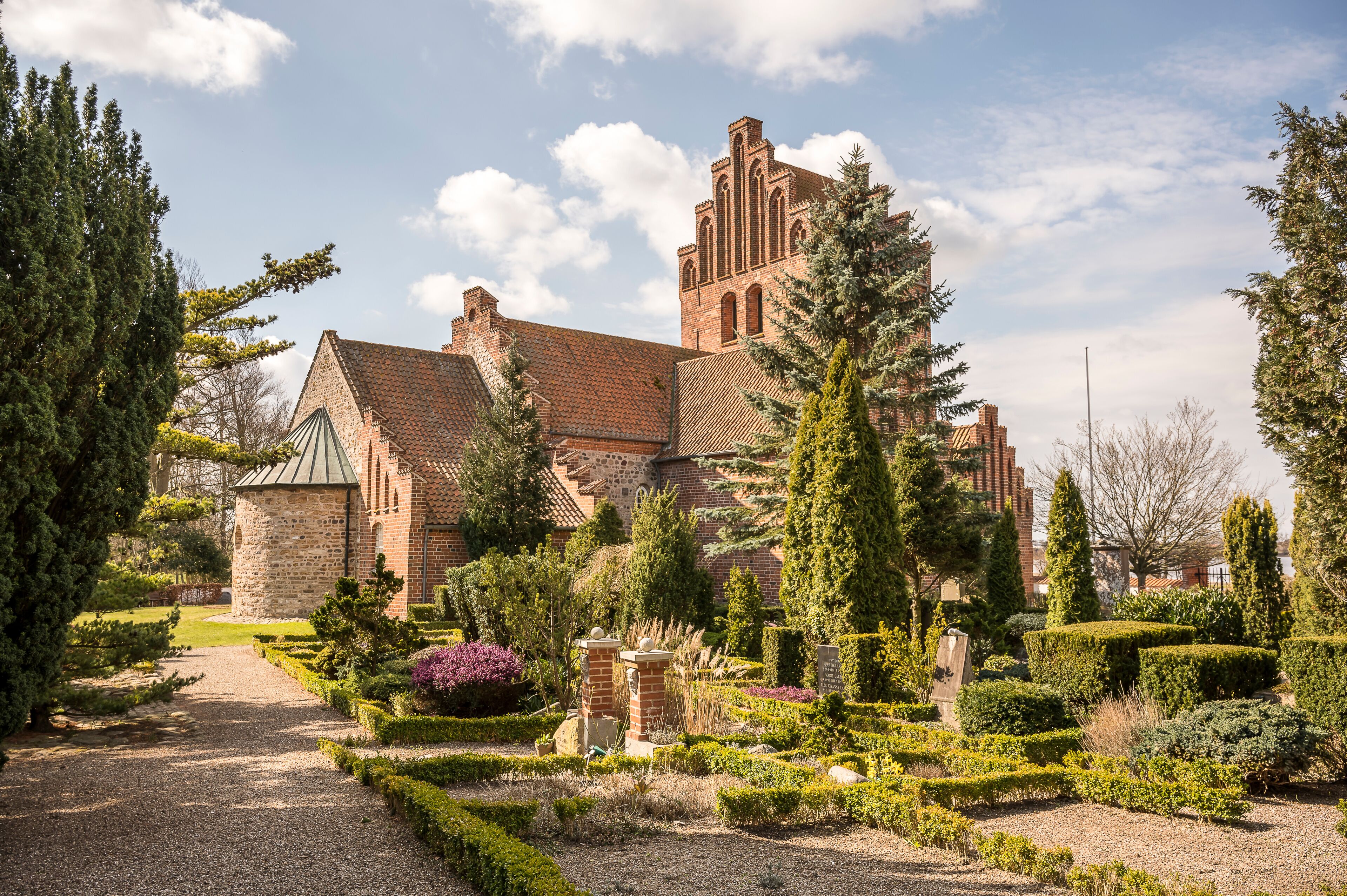 A historic brick building with a tower, surrounded by well-manicured gardens and tall trees.