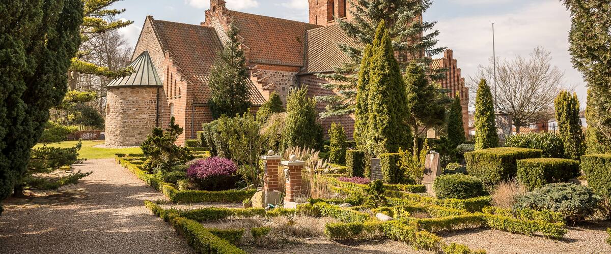 A historic brick building with a tower, surrounded by well-manicured gardens and tall trees.