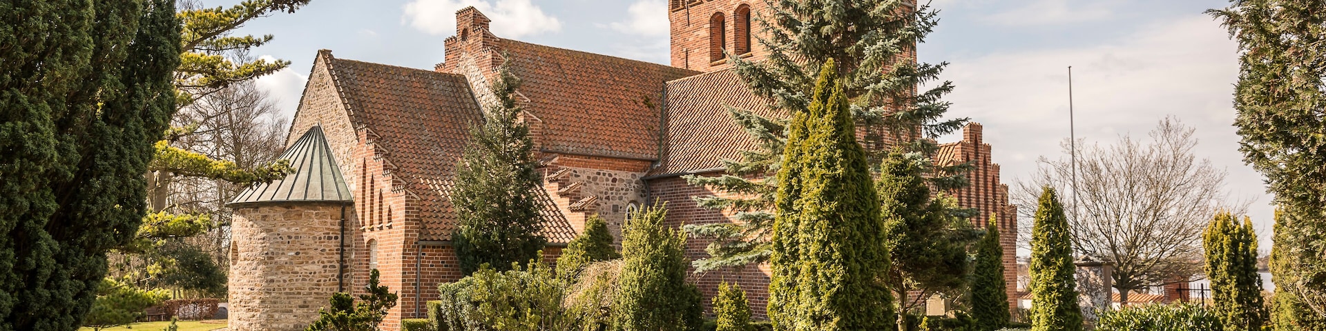 A historic brick building with a tower, surrounded by well-manicured gardens and tall trees.