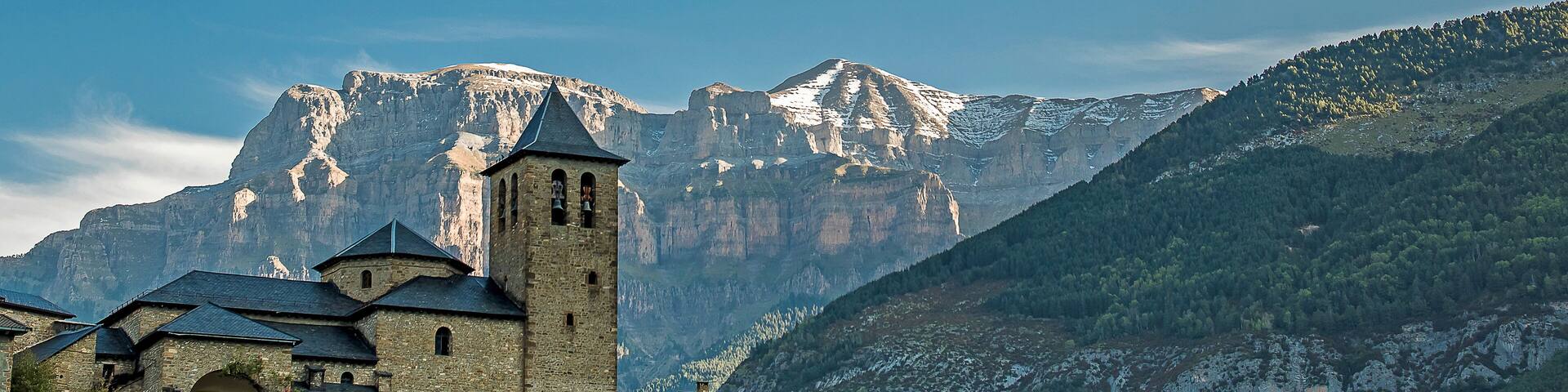 panoramic view of the church of san sebastian de torla and snow-capped mountains of the valley of ordesa in the background. Huesca pyrenees