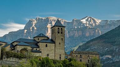 panoramic view of the church of san sebastian de torla and snow-capped mountains of the valley of ordesa in the background. Huesca pyrenees