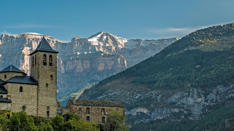 panoramic view of the church of san sebastian de torla and snow-capped mountains of the valley of ordesa in the background. Huesca pyrenees