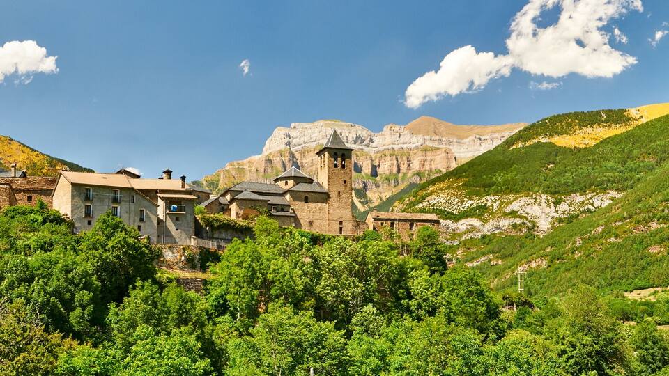 A mountainous village with stone buildings and a prominent church tower.
