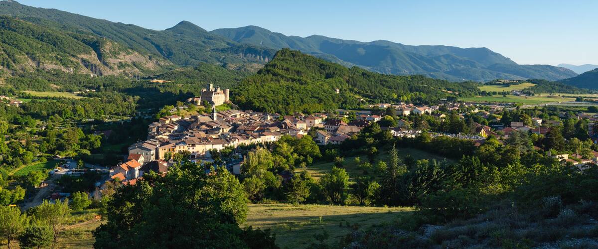 A town nestled in a valley surrounded by mountains, with a castle-like structure on a hill.