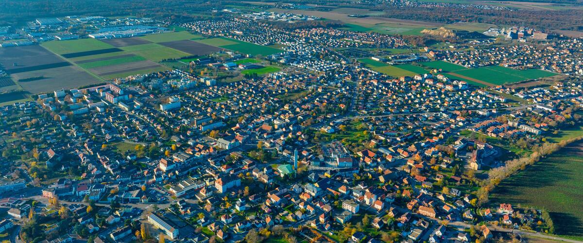 An aerial view of a densely populated town with a mix of residential houses and green fields, surrounded by mountains.