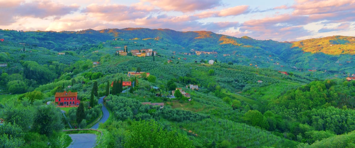 A lush green valley with scattered houses and a prominent red building.