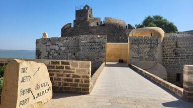 A historical fort with a paved entrance, stone walls, and a clear view of the sea.