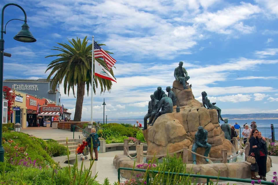 A coastal park with a statue of fishermen, a palm tree, and a view of the ocean.