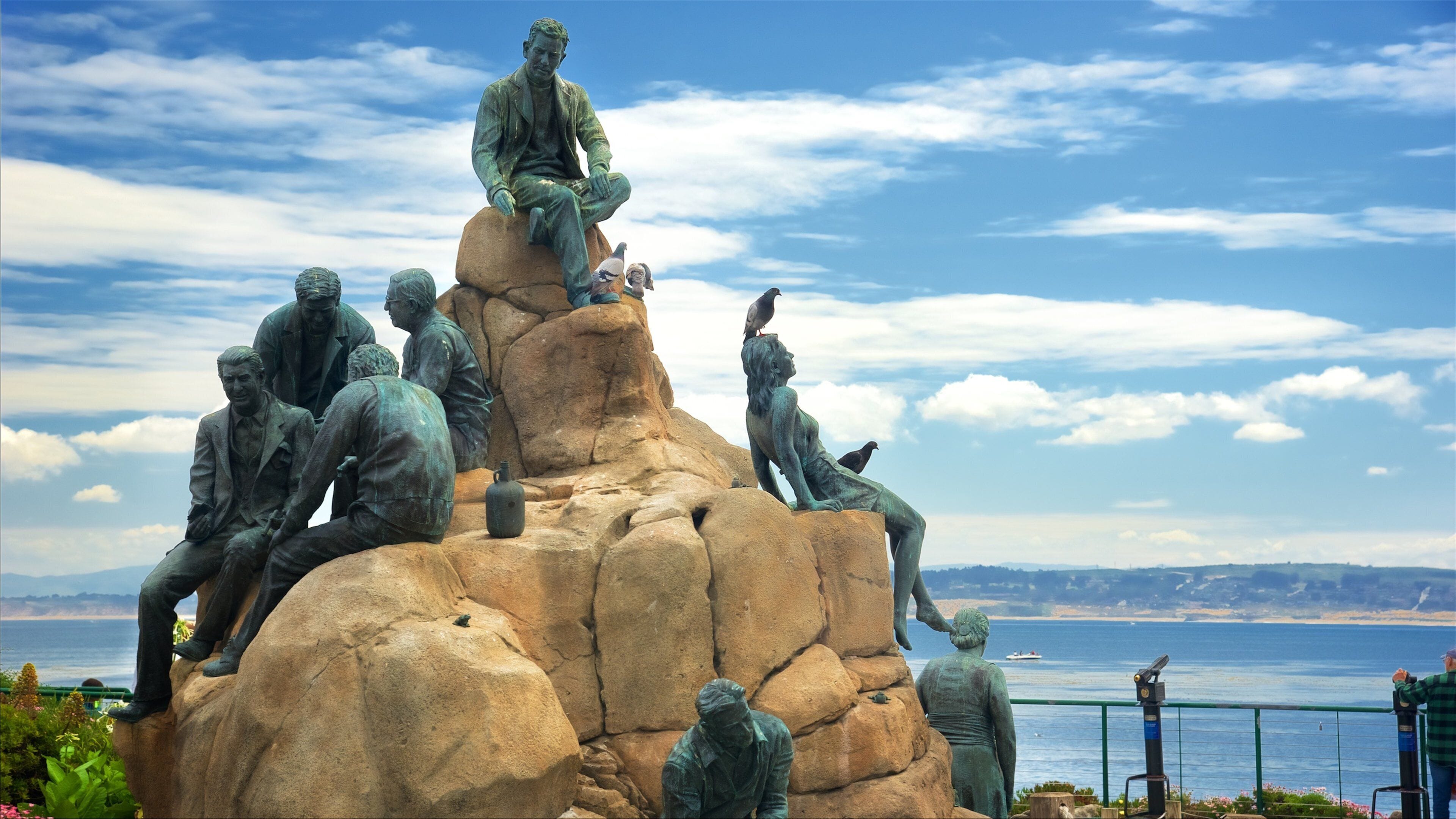 Escultura de personas sobre rocas con vista al mar.