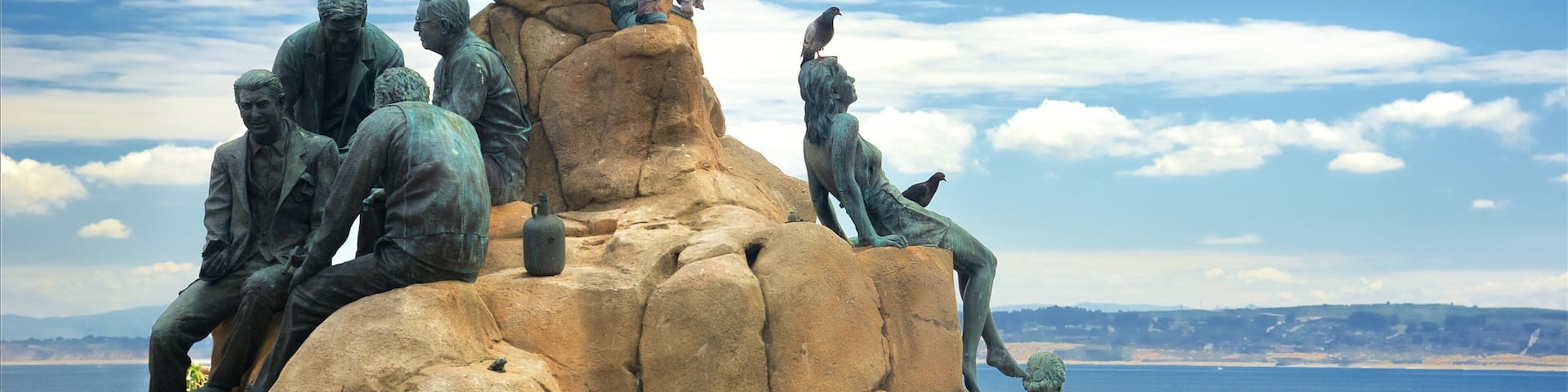 A sculpture of people on rocks with a view of the sea.