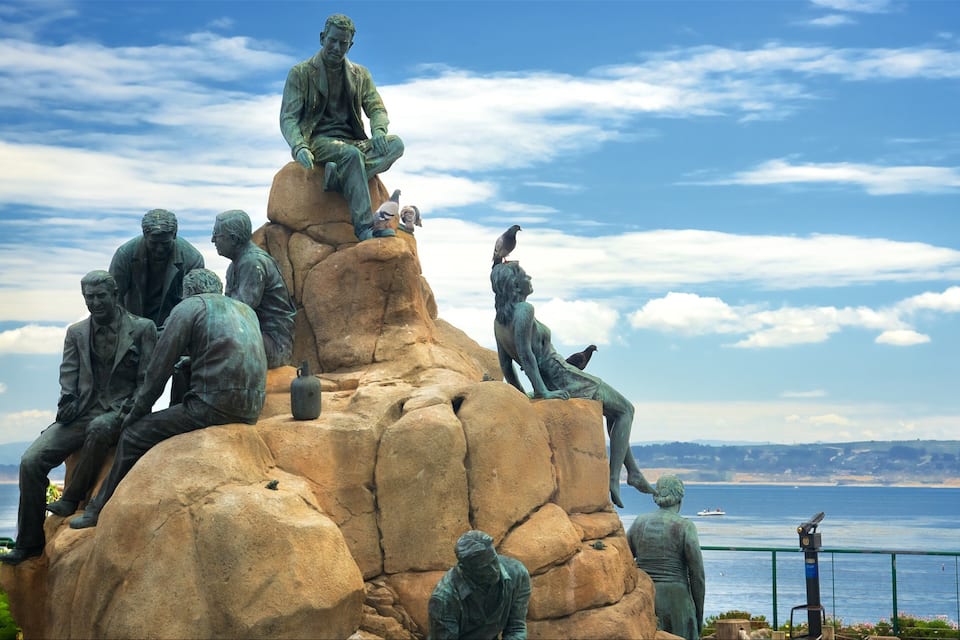 Escultura de personas sobre rocas con vista al mar.
